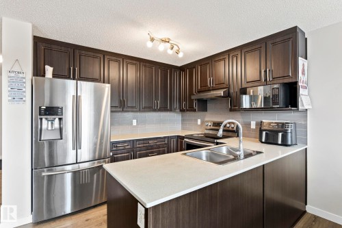 The kitchen features dark wood cabinetry, stainless steel appliances, a double basin sink, and light-colored countertops - 483 Ebbers Way Nw, Edmonton, AB - Indoor Photo Showing Kitchen With Double Sink