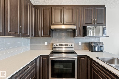 The kitchen features dark wood cabinetry, light-colored countertops, a tile backsplash, and stainless steel appliances including a range and range hood - 483 Ebbers Way Nw, Edmonton, AB - Indoor Photo Showing Kitchen