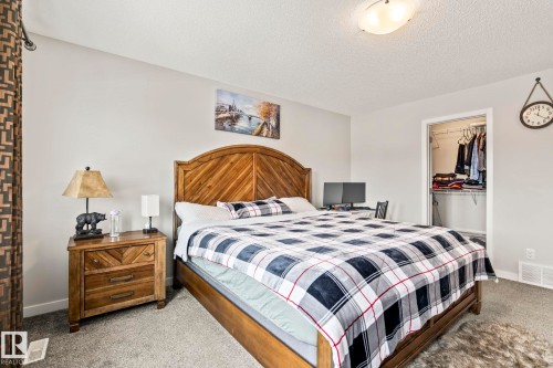 The bedroom features light-colored walls, carpeted flooring, and a wooden bed frame with a matching nightstand - 483 Ebbers Way Nw, Edmonton, AB - Indoor Photo Showing Bedroom