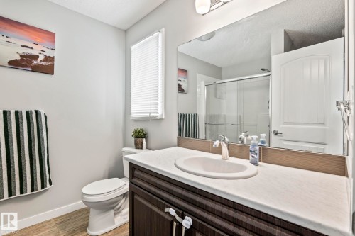 This bathroom features a vanity with a white countertop and a dark wood-look cabinet, a toilet, and a window with blinds - 483 Ebbers Way Nw, Edmonton, AB - Indoor Photo Showing Bathroom