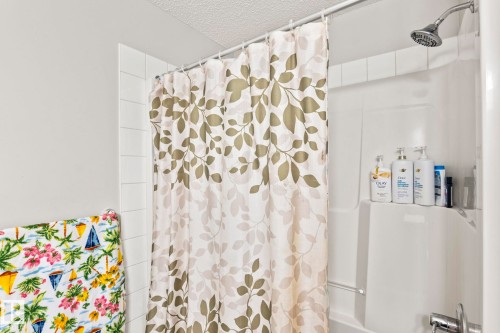 This bathroom features a shower with a shower head, white tiled walls, and a shower curtain with a leaf pattern - 483 Ebbers Way Nw, Edmonton, AB - Indoor Photo Showing Bathroom