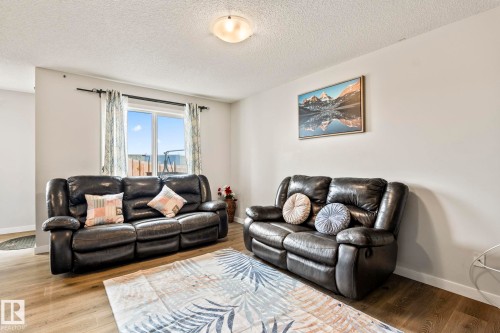 This living area features light-toned walls, a window with curtains providing natural light, and wood-look flooring - 483 Ebbers Way Nw, Edmonton, AB - Indoor Photo Showing Living Room