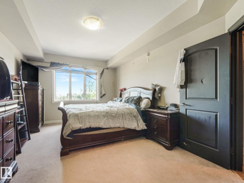 Bedroom featuring carpeted flooring, a large window providing natural light, and a dark wood door - 412 12408 15 Avenue, Edmonton, AB - Indoor Photo Showing Bedroom