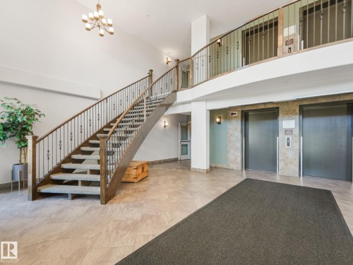 Spacious lobby featuring a grand staircase with ornate railings, tiled flooring, and dual elevators for convenient access - 412 12408 15 Avenue, Edmonton, AB - Indoor Photo Showing Other Room