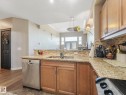 The kitchen features granite countertops, a tiled backsplash, and wooden cabinetry - 412 12408 15 Avenue, Edmonton, AB  - Indoor Photo Showing Kitchen With Double Sink 