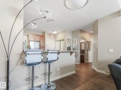 The property features hardwood floors, a kitchen area with wooden cabinetry and a stainless steel appliance, and a breakfast bar with seating - 