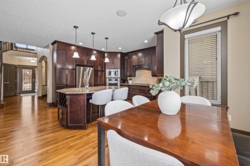 The property features a spacious open-concept kitchen and dining area with hardwood flooring, dark wood cabinetry, a large kitchen island with seating, and stainless steel appliances - 1014 Hope Road, Edmonton, AB - Indoor Photo Showing Dining Room