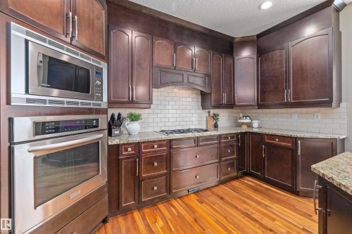 The kitchen features rich wood cabinetry, granite countertops, a subway tile backsplash, and stainless steel appliances including a built-in oven and microwave - 1014 Hope Road, Edmonton, AB - Indoor Photo Showing Kitchen