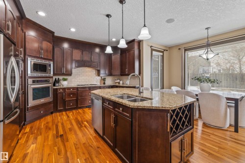 The kitchen features dark wood cabinetry, stainless steel appliances, and a granite-topped island with an integrated sink - 1014 Hope Road, Edmonton, AB - Indoor Photo Showing Kitchen With Double Sink With Upgraded Kitchen