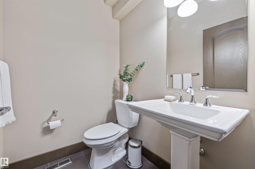 This bathroom features a pedestal sink with chrome fixtures, a toilet, a wall-mounted mirror, and tiled flooring - 1014 Hope Road, Edmonton, AB - Indoor Photo Showing Bathroom