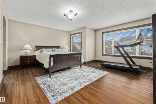 This Primary Bedroom features warm-toned hardwood flooring, light neutral-toned walls, and large windows with blinds - 1014 Hope Road, Edmonton, AB - Indoor Photo Showing Bedroom