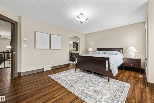 Primary Bedroom featuring rich wood flooring, a decorative area rug, and an arched entryway leading to a bathroom with a vanity visible - 1014 Hope Road, Edmonton, AB - Indoor Photo Showing Bedroom