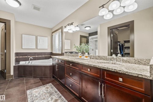 Primary Bathroom with a spacious built-in soaking tub, a double vanity featuring granite countertops and dark wood cabinetry, and a large mirror with integrated lighting - 1014 Hope Road, Edmonton, AB - Indoor Photo Showing Bathroom