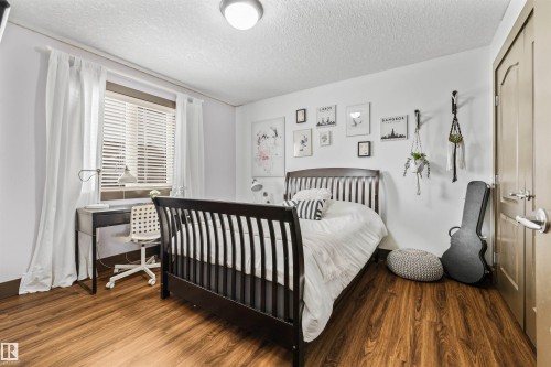 This room features warm-toned wood flooring and a window with blinds and white curtains - 1014 Hope Road, Edmonton, AB - Indoor Photo Showing Bedroom