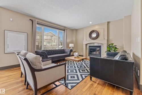 Living room featuring hardwood floors, a fireplace with a stone surround and mantle, and large windows providing ample natural light - 1014 Hope Road, Edmonton, AB - Indoor Photo Showing Living Room With Fireplace