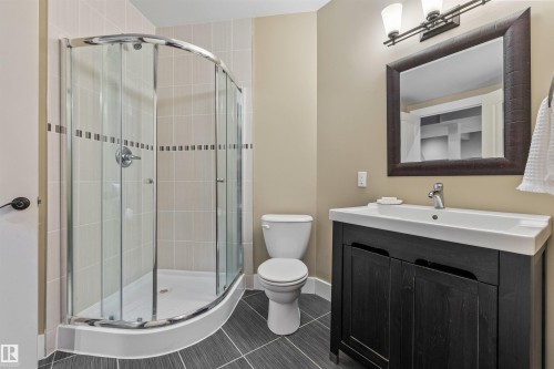 The bathroom features a curved glass shower enclosure, a toilet, a vanity with a dark wood cabinet, and a framed mirror above the vanity - 1014 Hope Road, Edmonton, AB - Indoor Photo Showing Bathroom