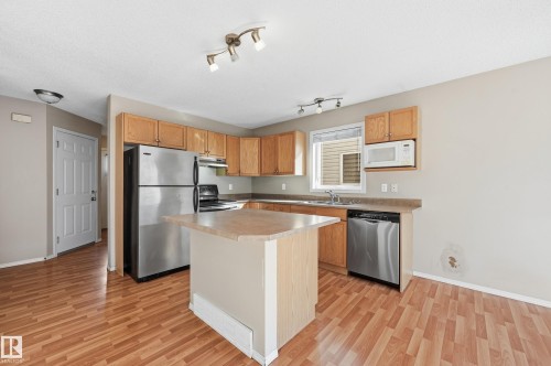 The kitchen features wood cabinetry, an island with a countertop, and stainless steel appliances including a refrigerator, stove, and dishwasher - 53 287 Macewan Road, Edmonton, AB - Indoor Photo Showing Kitchen With Stainless Steel Kitchen