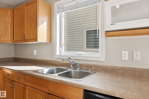 Kitchen featuring wood cabinetry, a stainless steel double sink, and a window with blinds - 53 287 Macewan Road, Edmonton, AB - Indoor Photo Showing Kitchen With Double Sink