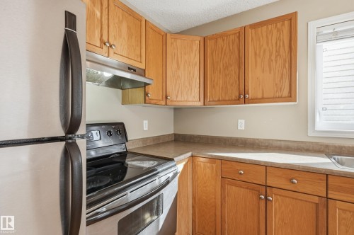 The kitchen features light wood cabinetry, a stainless steel refrigerator, and a stainless steel oven with a black cooktop - 53 287 Macewan Road, Edmonton, AB - Indoor Photo Showing Kitchen