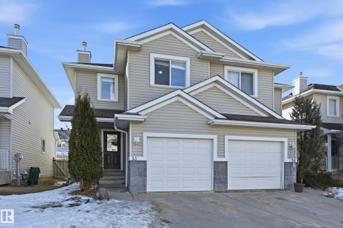 This property features a two-story exterior with light-colored siding, a dark front door, and a two-car garage - 53 287 Macewan Road, Edmonton, AB - Outdoor With Facade