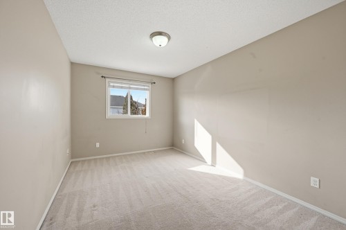 This room features a neutral color palette, plush carpeting, a window providing natural light, and a ceiling-mounted light fixture - 53 287 Macewan Road, Edmonton, AB - Indoor Photo Showing Other Room