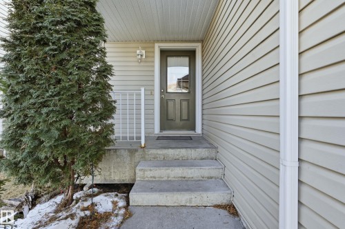 The property features a concrete front porch with steps, a dark-colored entry door with a glass insert, and light-colored siding - 53 287 Macewan Road, Edmonton, AB - Outdoor With Exterior