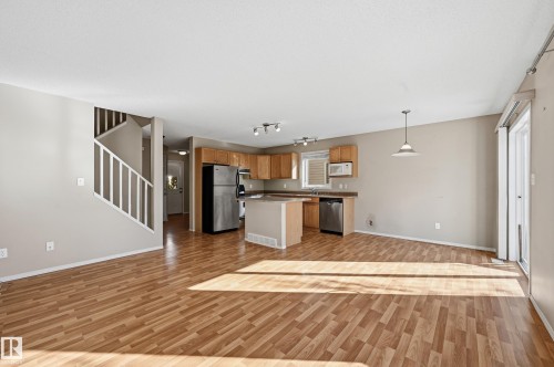 Open concept living area featuring wood-look flooring, light-colored walls, and a kitchen with wooden cabinetry and stainless steel appliances - 53 287 Macewan Road, Edmonton, AB - Indoor Photo Showing Kitchen