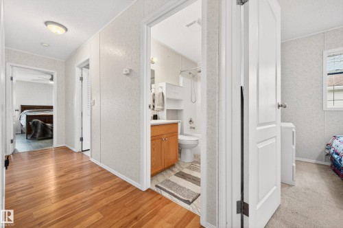 Hallway featuring hardwood flooring and a ceiling light fixture, with a view into a bathroom with a vanity and toilet, and another room beyond - 1727 Jubilee Loop, Sherwood Park, AB - Indoor