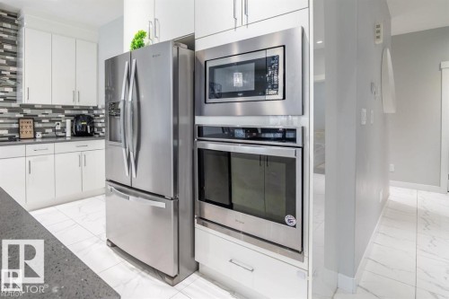 The kitchen features white cabinetry, stainless steel appliances including a refrigerator, microwave, and oven, and a tiled backsplash - 3608 46 Avenue, Beaumont, AB - Indoor Photo Showing Kitchen With Stainless Steel Kitchen