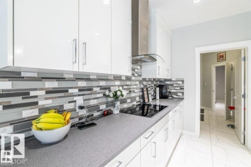 The kitchen features white cabinetry, a tiled backsplash with a mosaic pattern, and a cooktop with a stainless steel range hood - 3608 46 Avenue, Beaumont, AB - Indoor Photo Showing Kitchen With Upgraded Kitchen