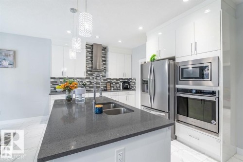 The kitchen features a spacious island with a double sink, stainless steel appliances, and sleek white cabinetry - 3608 46 Avenue, Beaumont, AB - Indoor Photo Showing Kitchen With Stainless Steel Kitchen With Double Sink With Upgraded Kitchen