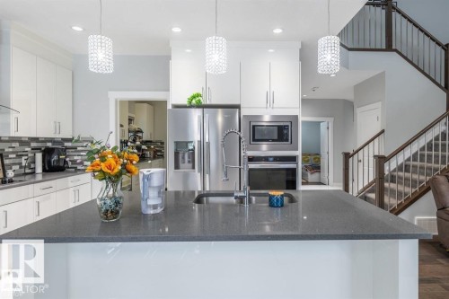 The kitchen features a spacious island with a sink, stainless steel appliances, white cabinetry, and a grey and white tiled backsplash - 3608 46 Avenue, Beaumont, AB - Indoor Photo Showing Kitchen With Stainless Steel Kitchen With Upgraded Kitchen
