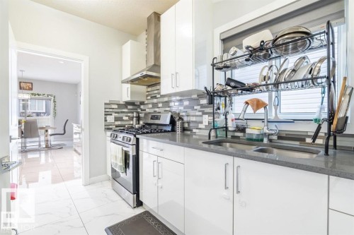 The kitchen features white cabinetry, a stainless steel gas range, a mosaic tile backsplash, and a double basin sink - 3608 46 Avenue, Beaumont, AB - Indoor Photo Showing Kitchen With Double Sink