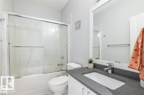 Bathroom featuring a vanity with a dark speckled countertop and a modern chrome faucet, a large framed mirror, and a shower with a sliding glass door - 3608 46 Avenue, Beaumont, AB - Indoor Photo Showing Bathroom
