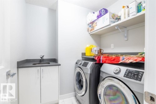 Dedicated laundry area featuring a sink with a dark countertop, white cabinetry, and wall-mounted shelving - 3608 46 Avenue, Beaumont, AB - Indoor Photo Showing Laundry Room
