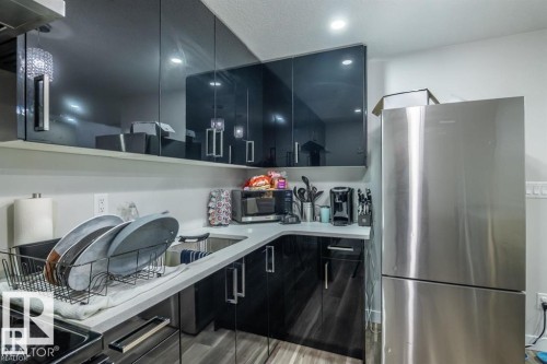 The kitchen features sleek black cabinetry, light-colored countertops, and a stainless steel refrigerator - 3608 46 Avenue, Beaumont, AB - Indoor Photo Showing Kitchen With Stainless Steel Kitchen