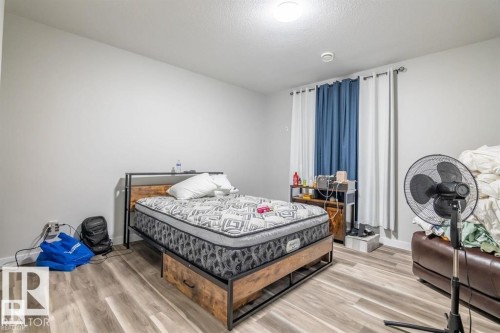Bedroom with light gray walls, hardwood style flooring, and a window with white and blue curtains - 3608 46 Avenue, Beaumont, AB - Indoor Photo Showing Bedroom