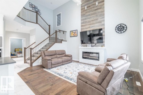 Expansive living area featuring high ceilings, hardwood flooring, an elegant staircase with wood railings, and a contemporary fireplace with a decorative wood panel accent - 3608 46 Avenue, Beaumont, AB - Indoor Photo Showing Living Room With Fireplace
