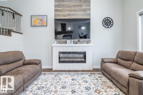 Living area featuring hardwood flooring, a modern fireplace with a tiled surround and wood paneling, and a staircase with metal railings - 3608 46 Avenue, Beaumont, AB - Indoor Photo Showing Living Room With Fireplace