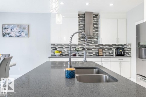 Modern kitchen featuring white cabinetry, a unique tile backsplash, stainless steel appliances, and a kitchen island with a double sink - 3608 46 Avenue, Beaumont, AB - Indoor Photo Showing Kitchen With Double Sink