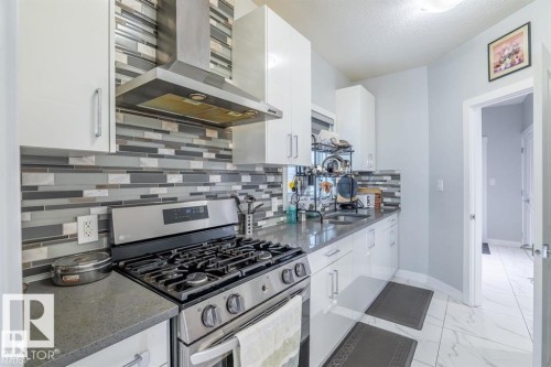 The kitchen features white cabinetry, a stainless steel gas range, a coordinating stainless steel range hood, and a striking mosaic tile backsplash - 3608 46 Avenue, Beaumont, AB - Indoor Photo Showing Kitchen With Upgraded Kitchen
