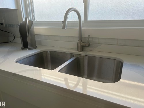 The kitchen features a double basin stainless steel sink with a gooseneck faucet, set within a white countertop, and complemented by a white subway tile backsplash - 14911 77 Street Nw, Edmonton, AB - Indoor Photo Showing Kitchen With Double Sink