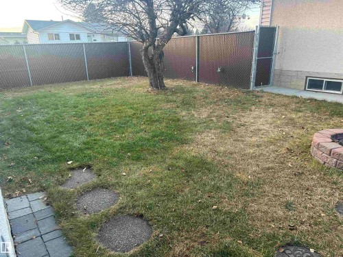 The property features a fenced yard with a combination of grass and paved sections, complete with a brick-built fire pit - 14911 77 Street Nw, Edmonton, AB - Outdoor