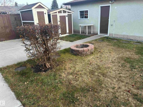 The property features a backyard with a lawn, two storage sheds, and a brick fire pit - 14911 77 Street Nw, Edmonton, AB - Outdoor