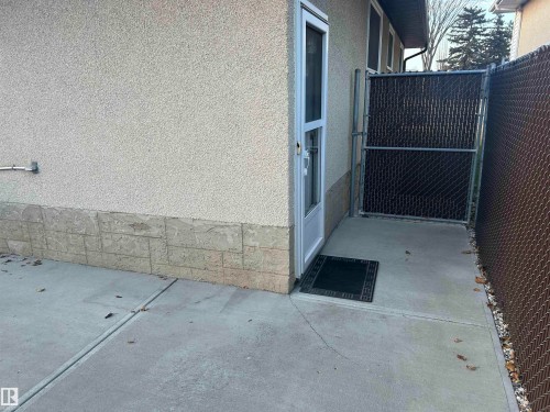 The property features a stucco exterior with a stone-look foundation, a concrete patio, and a chain link fence - 14911 77 Street Nw, Edmonton, AB - Outdoor