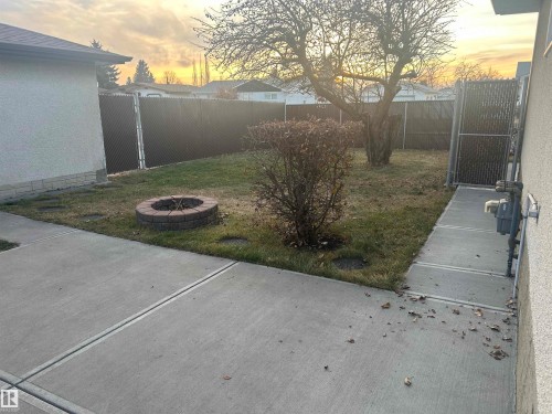The property features a yard with a paved patio area, a brick fire pit, and mature trees - 14911 77 Street Nw, Edmonton, AB 