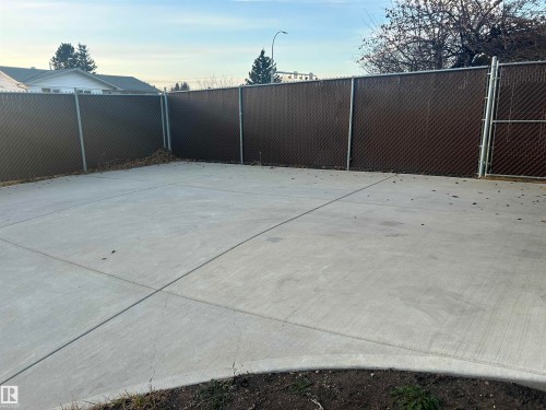 The property features a concrete paved area, enclosed by a chain-link fence with privacy slats, providing an outdoor space - 14911 77 Street Nw, Edmonton, AB - Outdoor