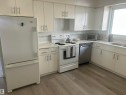 The kitchen features light-colored flooring, white cabinetry with silver-toned hardware, a white range, and a stainless steel dishwasher - 14911 77 Street Nw, Edmonton, AB  - Indoor Photo Showing Kitchen 