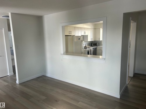 Living area with light-toned flooring, white walls, and a pass-through opening to the kitchen - 14911 77 Street Nw, Edmonton, AB - Indoor Photo Showing Other Room
