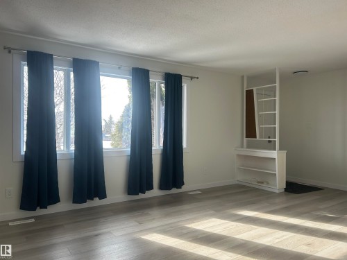 Spacious interior featuring large windows with dark curtains, light-colored walls, and wood-look flooring - 14911 77 Street Nw, Edmonton, AB - Indoor
